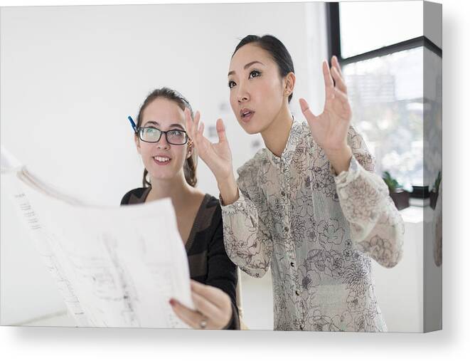 Working Canvas Print featuring the photograph Two female colleagues discussing blueprint by Steve Prezant