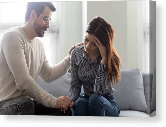 Young Men Canvas Print featuring the photograph Unhappy stressed woman sitting on sofa with empathic husband. by Fizkes