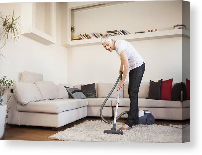 Working Canvas Print featuring the photograph Woman cleaning carpet with a vacuum cleaner in room by Vesna Andjic