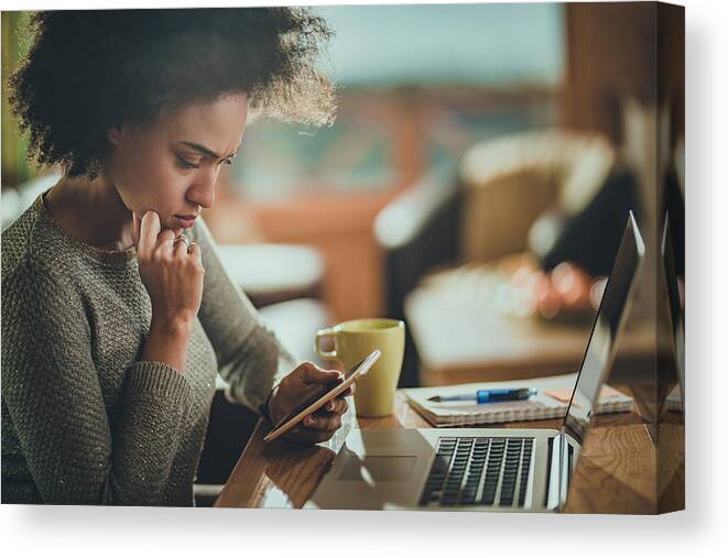 People Canvas Print featuring the photograph Worried African American woman using cell phone while working at home. by Skynesher