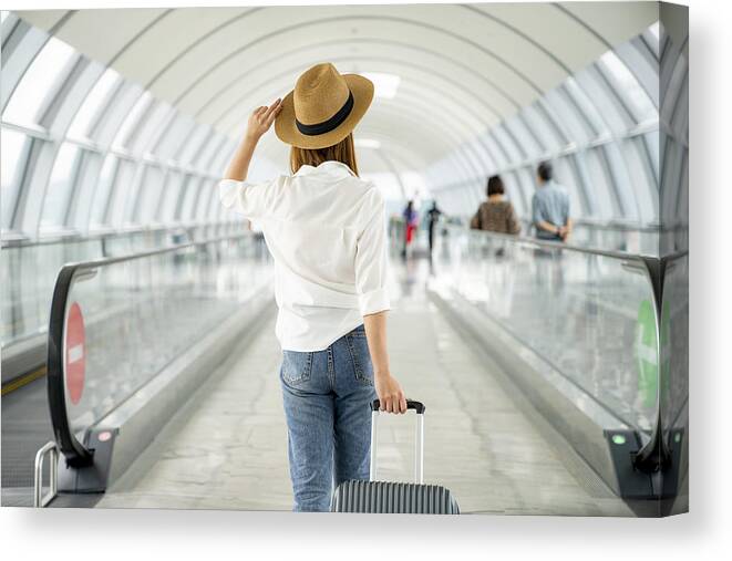 Wind Canvas Print featuring the photograph Young casual female traveler with suitcase at airport by Virojt Changyencham