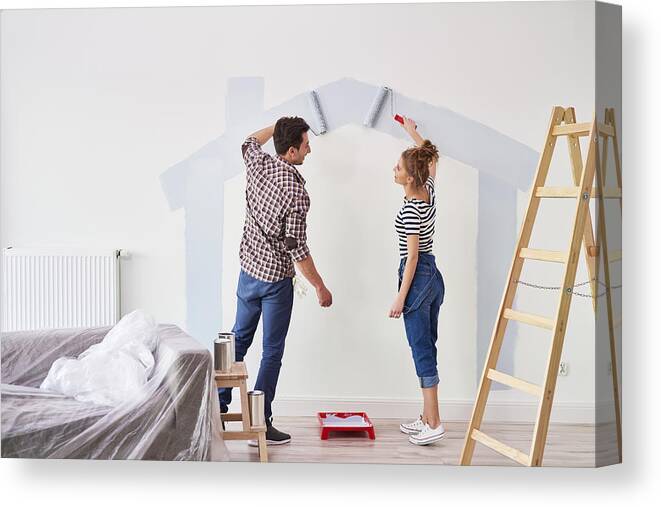 Working Canvas Print featuring the photograph Young couple painting the interior wall in their new apartment by Gpointstudio