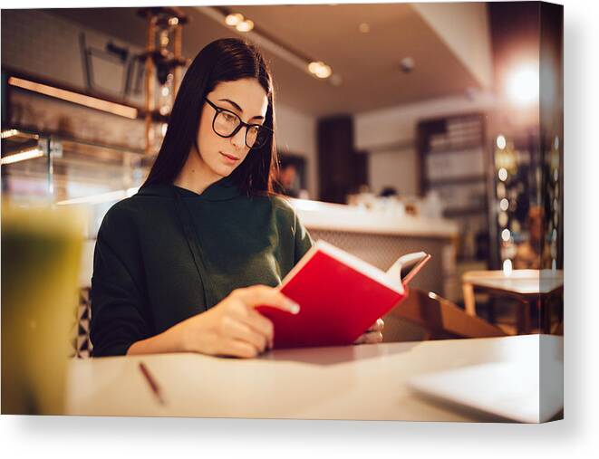 Hipster Culture Canvas Print featuring the photograph Young hipster woman reading a book at urban coffee shop by Wundervisuals