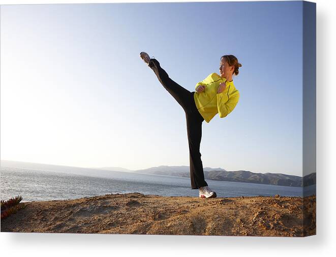 Standing On One Leg Canvas Print featuring the photograph Young woman practicing high kick on shore by Marcy Maloy