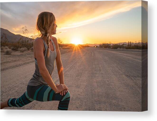 Focus Canvas Print featuring the photograph Young woman stretching body after jogging, sunset at the end of the road; female stretches body in nature by Swissmediavision
