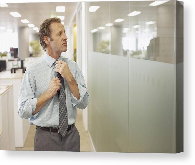 Corporate Business Canvas Print featuring the photograph Businessman adjusting tie in office by Paul Bradbury