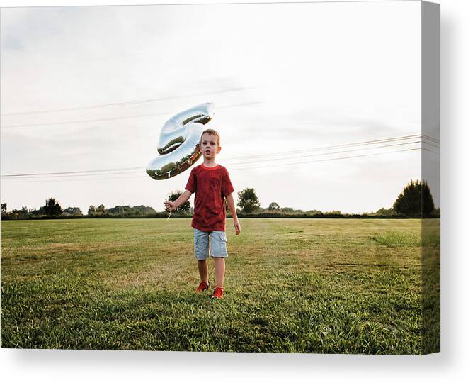 Boy Canvas Print featuring the photograph Boy Holding Number 5 Balloon While Walking On Grassy Field Against Sky by Cavan Images