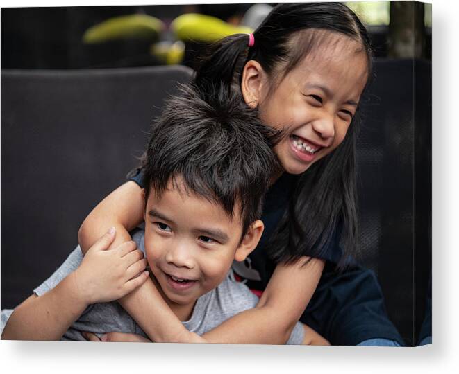 Siblings Canvas Print featuring the photograph Picture Of Two Young Thai Siblings Playfully Embrace by Cavan Images