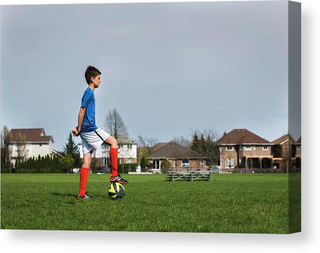 Side View Of Boy Kicking Soccer Ball While Playing On Grassy Field
