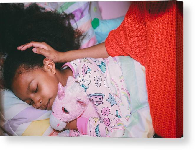 Child Canvas Print featuring the photograph Afrolatina girl in pajamas holding stuffed unicorn with her eyes closed. Mother's face and neck not visible. Mother's hand on daughters head. by Evelyn Martinez