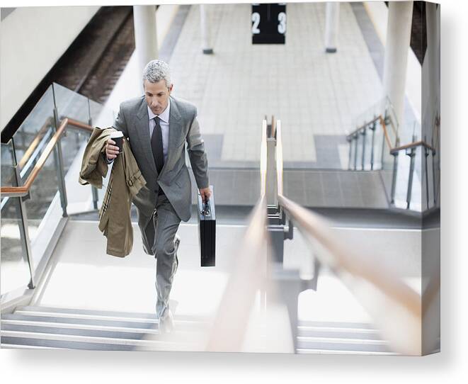 Mature Adult Canvas Print featuring the photograph Businessman walking up stairs in train station by Paul Bradbury