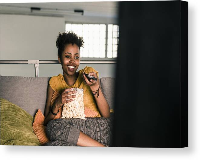 20-29 Years Canvas Print featuring the photograph Laughing young woman sitting on couch watching Tv by Westend61