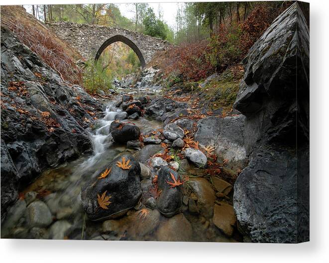 Autumn Canvas Print featuring the photograph Medieval stoned bridge with water flowing in the river in autumn. by Michalakis Ppalis