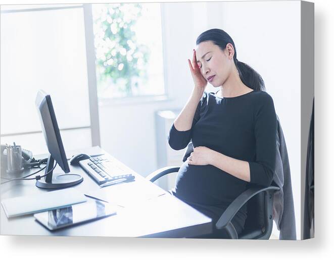 Horizontal Canvas Print featuring the photograph Tired pregnant Japanese businesswoman at desk by JGI/Tom Grill
