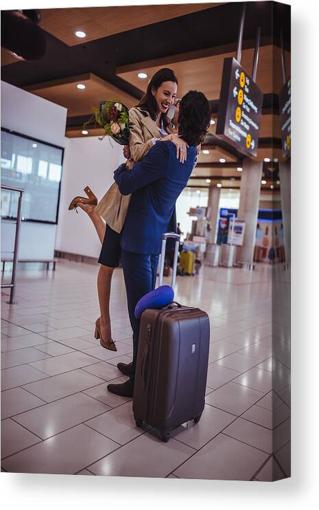 Young Men Canvas Print featuring the photograph Excited young man welcoming girlfriend with flowers at airport by Wundervisuals