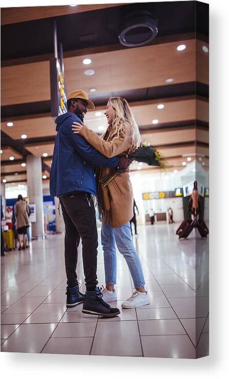20-29 Years Canvas Print featuring the photograph Young multi-ethnic friends meeting and embracing at airport by Wundervisuals
