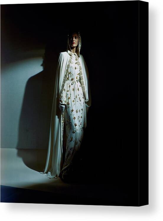 Fashion Canvas Print featuring the photograph A Model Wearing A Hooded Ivory Cape Over An Ivory by Horst P. Horst