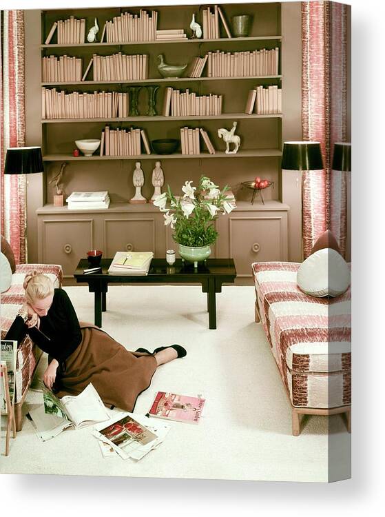 Home Interior Design Interior Literary Crafts One Person People Female Indoors Young Woman Young Adult Young Adult Woman Sitting Flowers Bouquet Bookshelf Book Sofa Furniture Coffee Table Reading Magazine Carpet Skirt #condenasthouse&gardenphotograph November 1st 1951 Canvas Print featuring the photograph A Woman Reading Magazines On The Floor by Haanel Cassidy