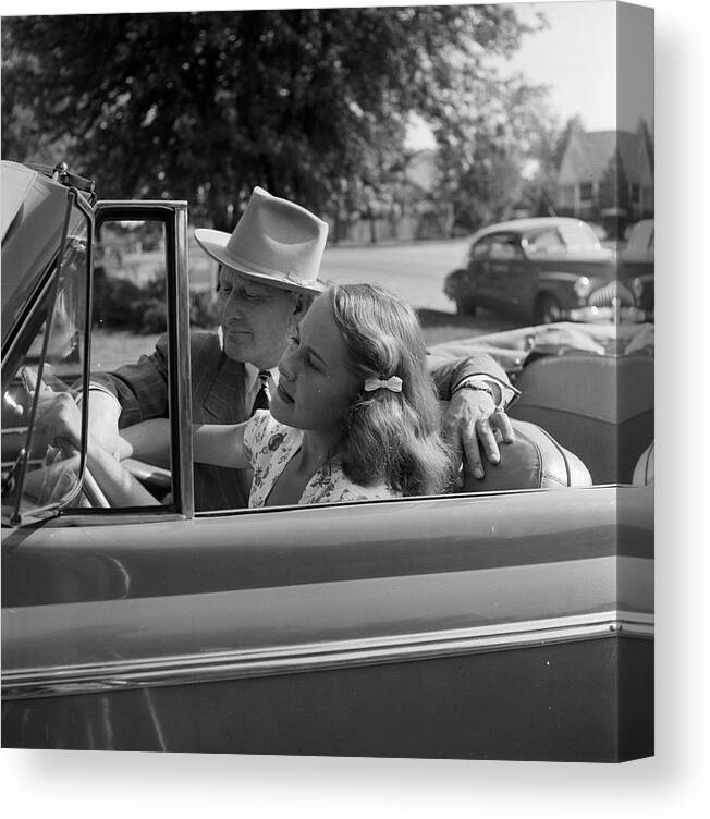 Archival Canvas Print featuring the photograph A teenage girl sitting behind the wheel of a car while an unidentified man is sitting nearby in Tulsa, OK in 1947. by Nina Leen