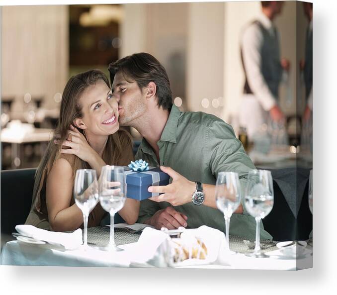 Heterosexual Couple Canvas Print featuring the photograph Man kissing and giving gift to woman in restaurant by Chris Ryan