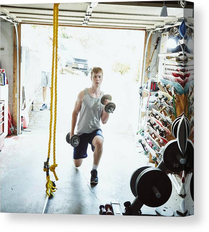Young Men Canvas Print featuring the photograph Young man doing lunges with dumbbells in gym in garage by Thomas Barwick