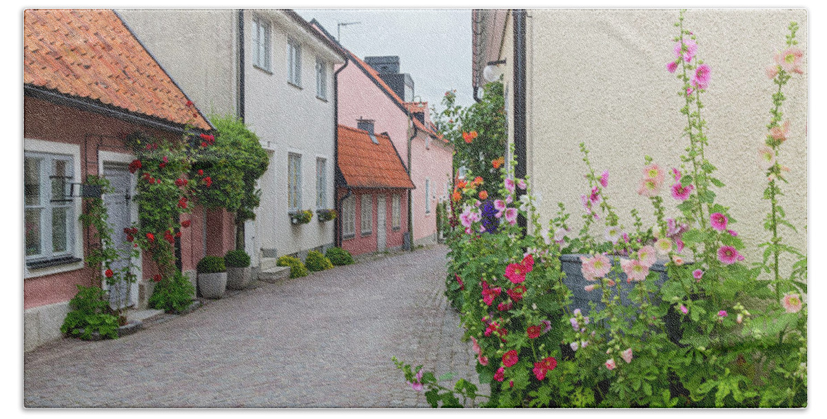 Street Bath Towel featuring the photograph Cozy street with blooming mallows and roses by GoodMood Art