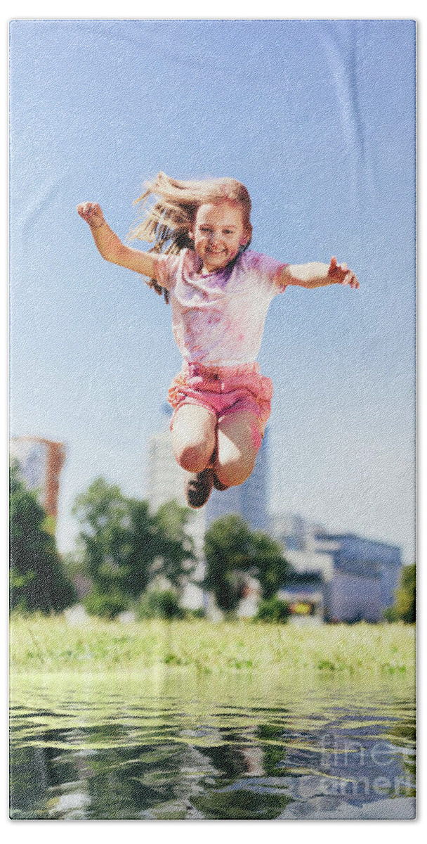 Little girl jumping high above big puddle of water. Bath Towel by