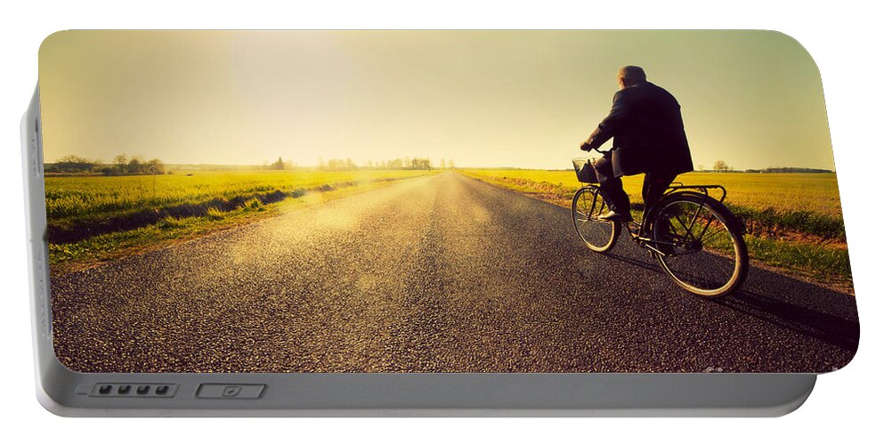 Road Portable Battery Charger featuring the photograph Old man riding a bike to sunny sunset sky by Michal Bednarek