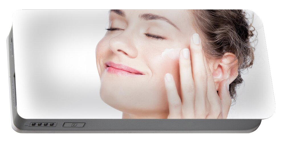 Skincare Portable Battery Charger featuring the photograph Beautiful young woman smiling and applying eye cream. by Michal Bednarek