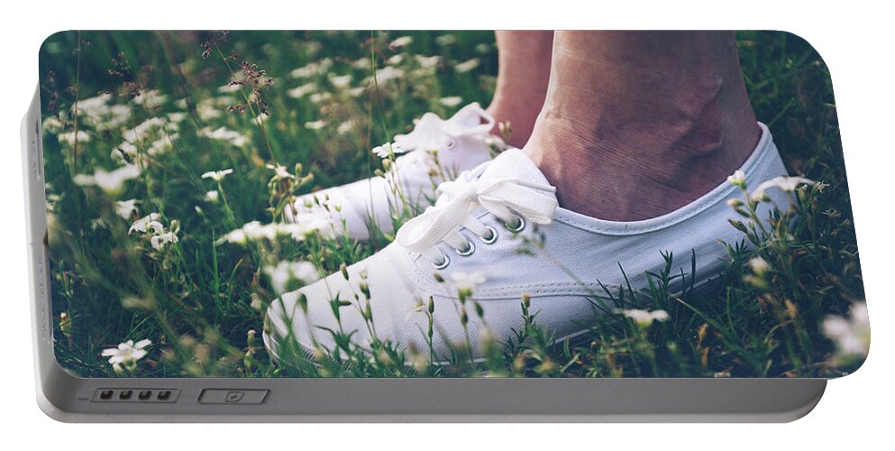 Woman Portable Battery Charger featuring the photograph Woman in sneakers standing on meadow with flowers. by Michal Bednarek