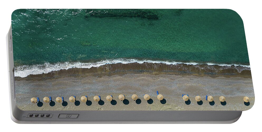 Summertime Portable Battery Charger featuring the photograph Aerial view from a flying drone of beach umbrellas in a row on an empty beach with braking waves. by Michalakis Ppalis