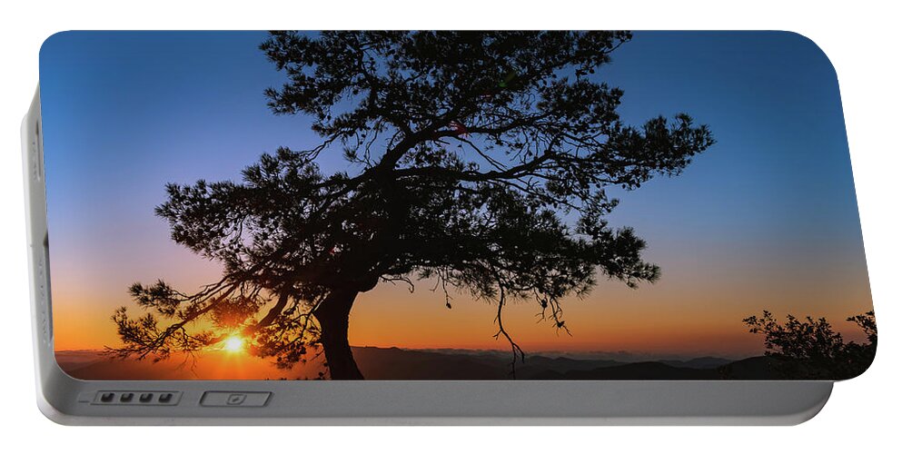 Cyprus Portable Battery Charger featuring the photograph Silhouette of a forest pine tree during blue hour with bright sun at sunset. by Michalakis Ppalis