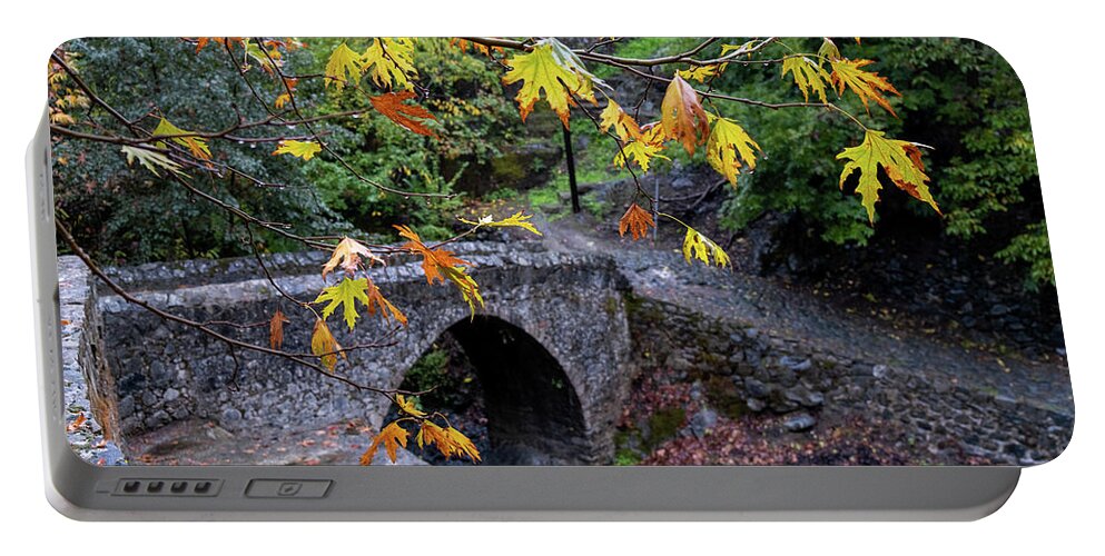 River Portable Battery Charger featuring the photograph Medieval stoned bridge water flowing in the river in autumn. by Michalakis Ppalis