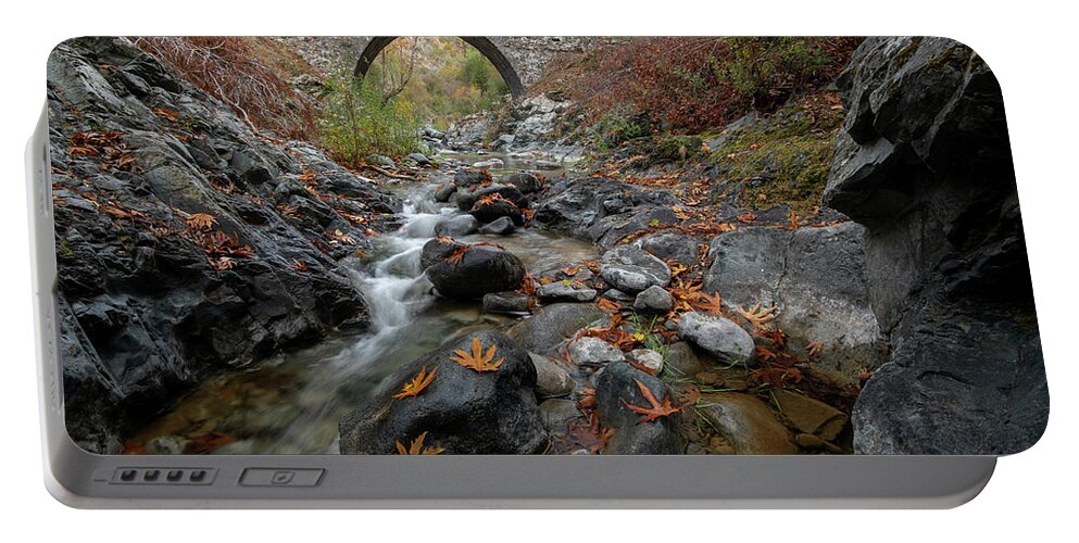 Autumn Portable Battery Charger featuring the photograph Medieval stoned bridge with water flowing in the river in autumn. by Michalakis Ppalis