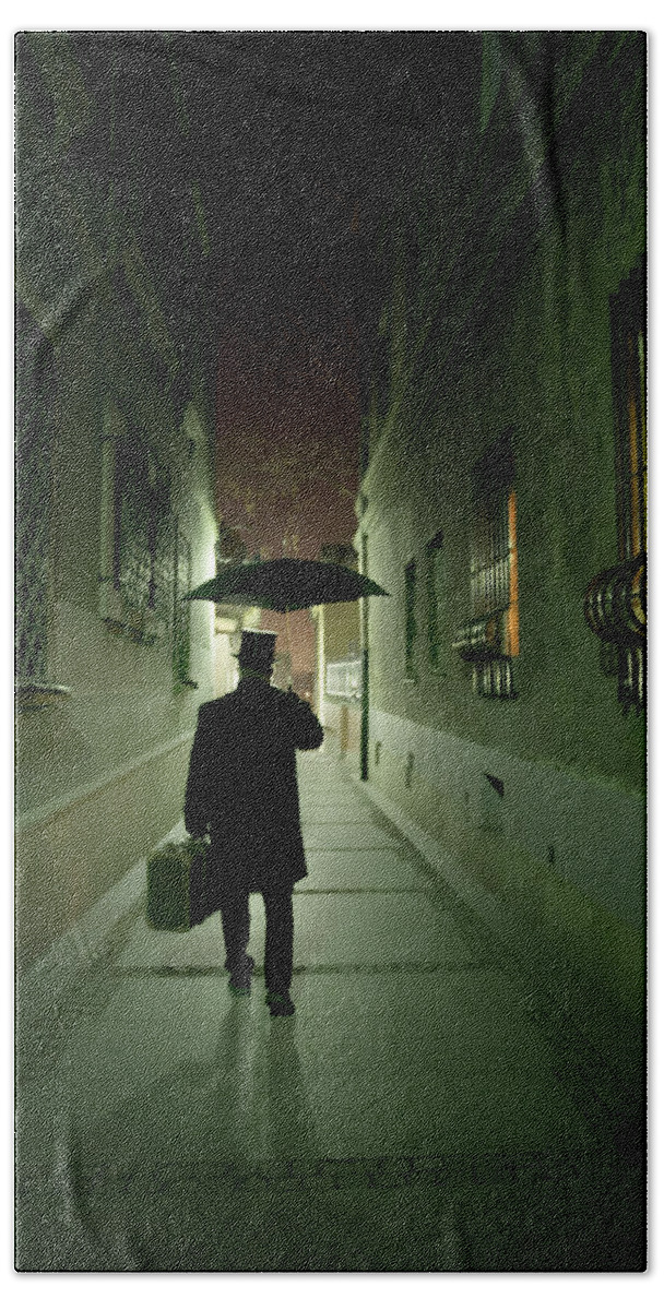 1800 S Beach Towel featuring the photograph Victorian man with top hat carrying a suitcase and umbrella walking in the narrow street at night by Jaroslaw Blaminsky