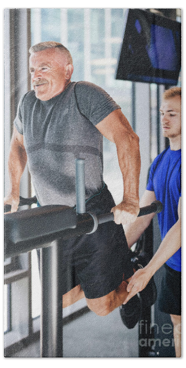 Man Beach Towel featuring the photograph Gym instructor helping senior man at the gym. by Michal Bednarek