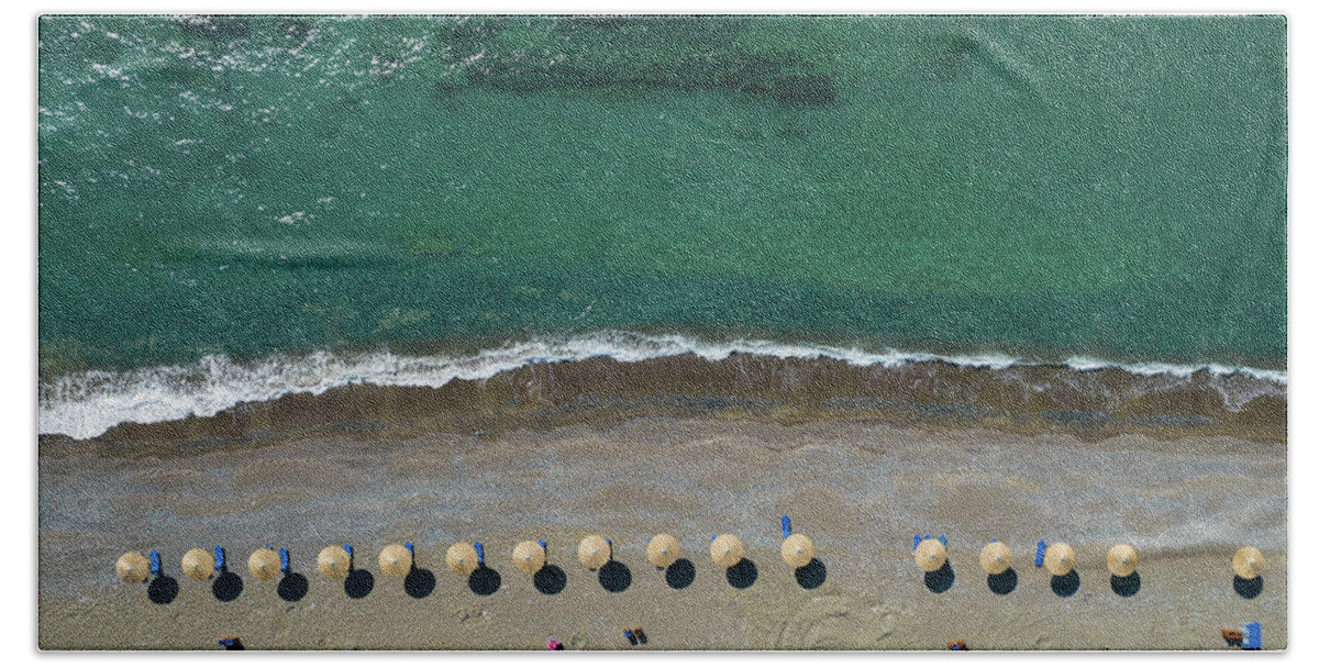 Summertime Beach Towel featuring the photograph Aerial view from a flying drone of beach umbrellas in a row on an empty beach with braking waves. by Michalakis Ppalis