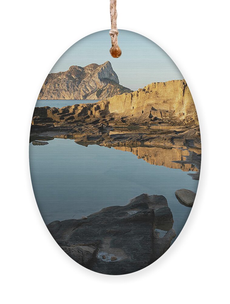 Mediterranean Ornament featuring the photograph Reflection of rocks in the calm Mediterranean Sea at sunrise 1 by Adriana Mueller