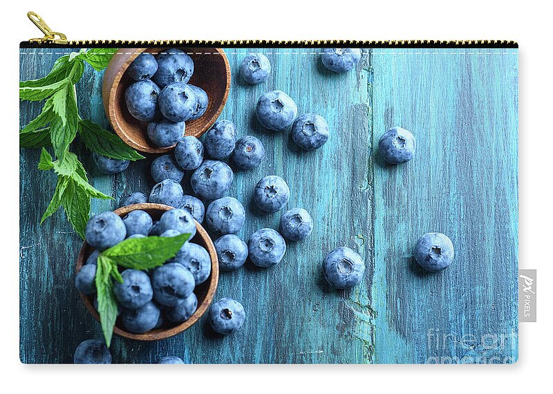 Blueberries Zip Pouch featuring the photograph Bowl of fresh blueberries on blue rustic wooden table from above by Jelena Jovanovic