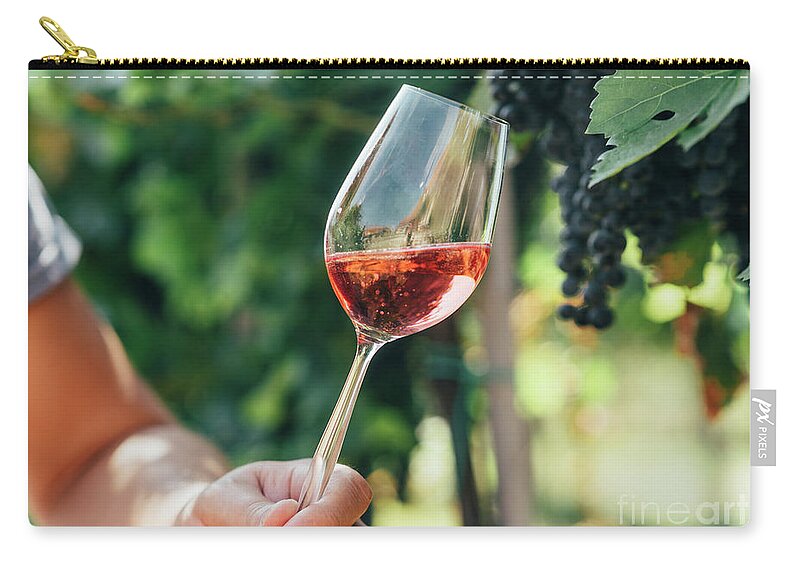 Wine Zip Pouch featuring the photograph Man holding glass of red wine in vineyard field. Wine tasting in #1 by Jelena Jovanovic