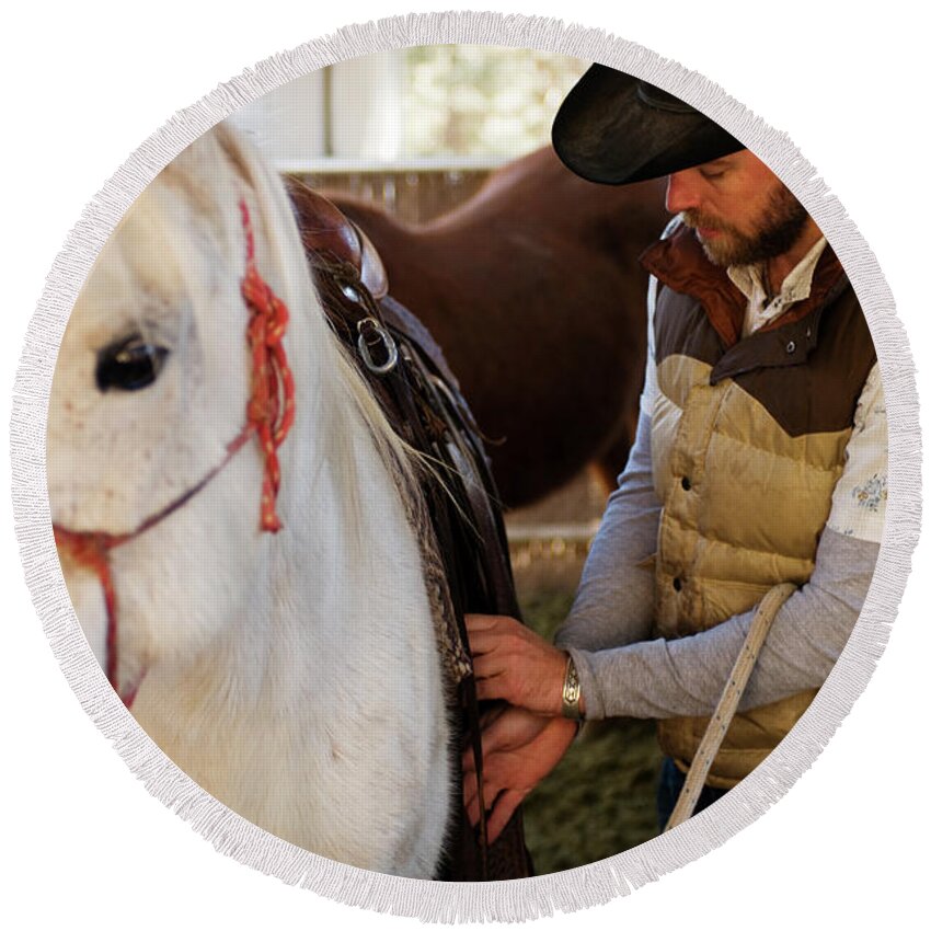 30s Round Beach Towel featuring the photograph A Male Ranch Hand Adjusts The Saddle by Kyle George
