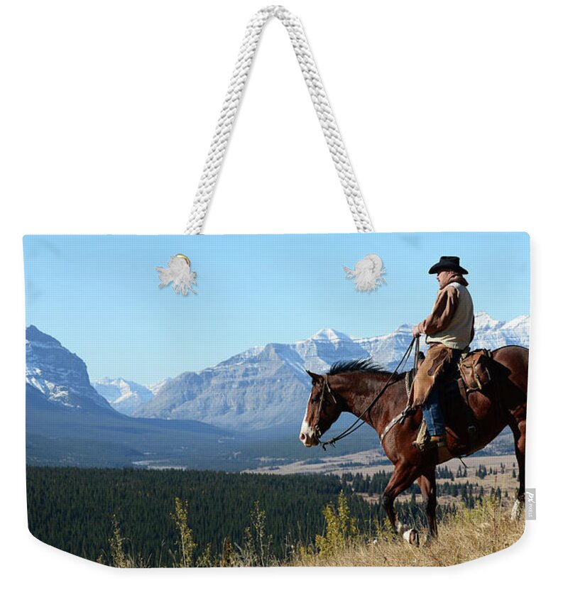 Cowboy Weekender Tote Bag featuring the photograph Cowboy Riding With A View Of The Rocky by Deb Garside