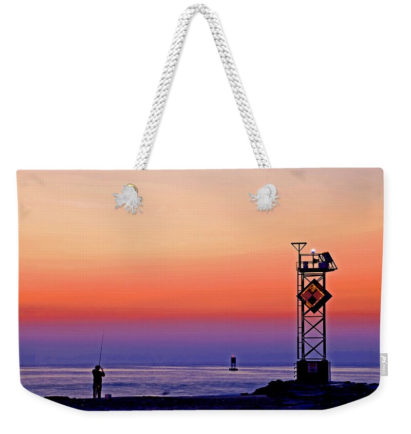 Ocean Water Seashore Beach Seaside Dawn Daybreak Sunrise Sky Pastel Colors Fishing Casting Fisherman Sport Recreation Fun Relaxation Clam Quiet Peaceful Contemplation Solitude Jetty Breakwater Rocks Tower Lights Warning Buoy Nature Weekender Tote Bag featuring the photograph Fishing near the Ocean City jetty by Bill Jonscher