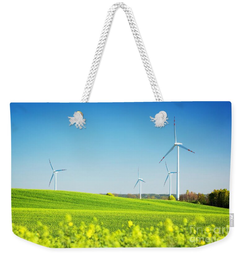 Wind Weekender Tote Bag featuring the photograph Wind turbines on spring field by Michal Bednarek