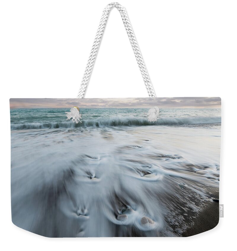Coastline Weekender Tote Bag featuring the photograph Pebbles in the beach and flowing sea water by Michalakis Ppalis