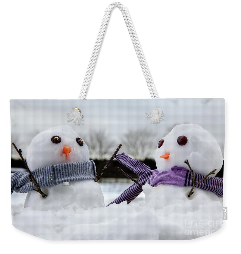Snowmen Weekender Tote Bag featuring the photograph Two cute snowmen wearing scarfs and twigs for arms by Simon Bratt