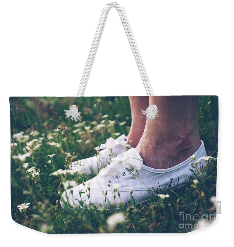 Woman Weekender Tote Bag featuring the photograph Woman in sneakers standing on meadow with flowers. by Michal Bednarek