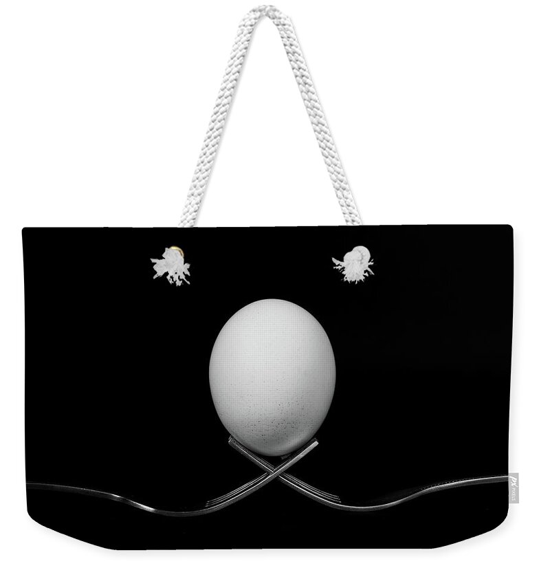 Egg Weekender Tote Bag featuring the photograph White egg resting on two metal and shiny forks on a black backg #1 by Michalakis Ppalis