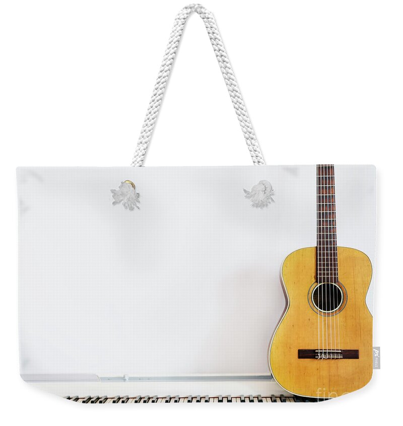 Guitar Weekender Tote Bag featuring the photograph Acoustic guitar on piano keyboard in front of white wall. by Jelena Jovanovic