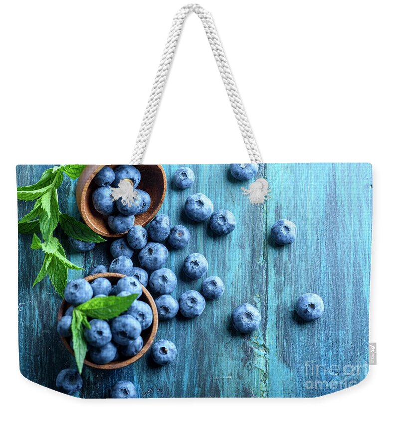Blueberries Weekender Tote Bag featuring the photograph Bowl of fresh blueberries on blue rustic wooden table from above by Jelena Jovanovic